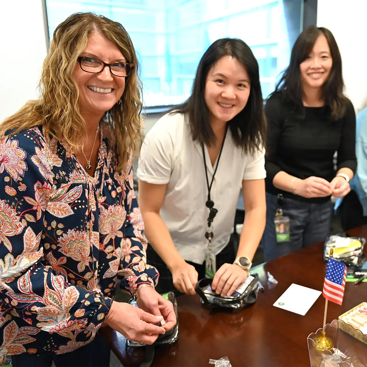 Three female colleagues smiling and assembling team kits in a conference room