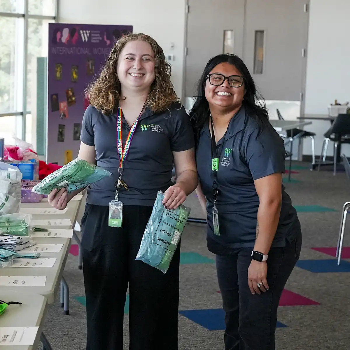 Two female colleagues smiling and assembling team kits in a conference room